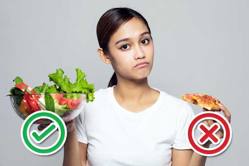 Young woman looking perplexed and sad holding a bowl full of green veggies in one hand and a slice of pizza in the other